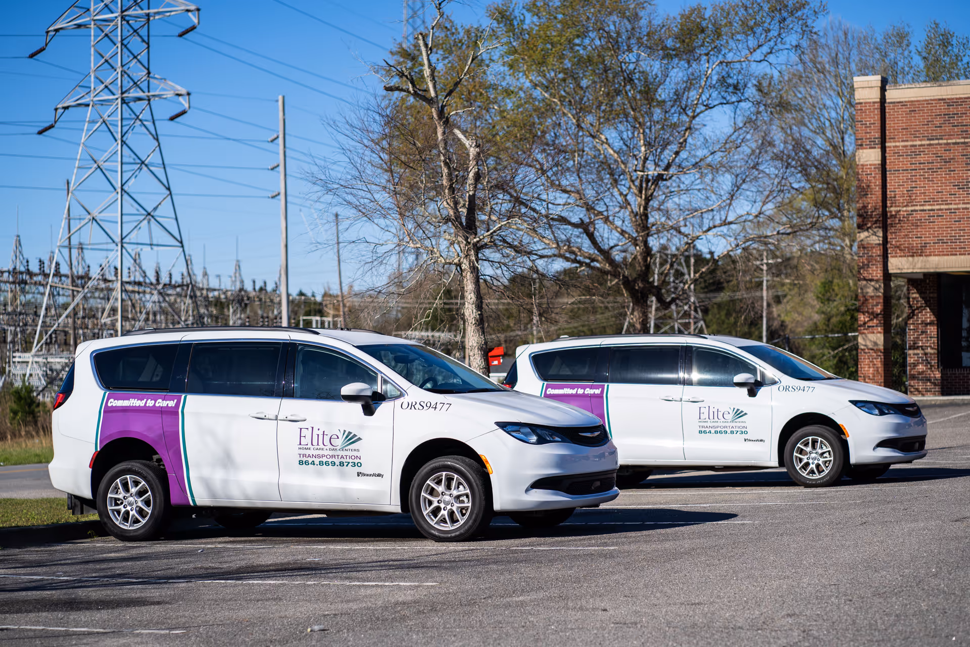 Two white Elite Home Care vans parked in a lot beside a brick building.