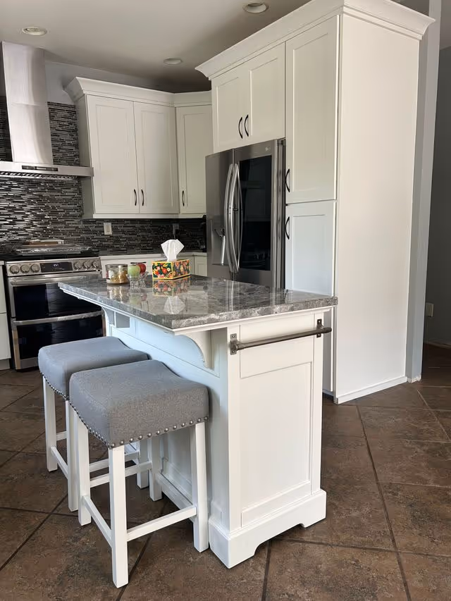 Bright white kitchen with an island, gray stools, stainless appliances, and tiled flooring.
