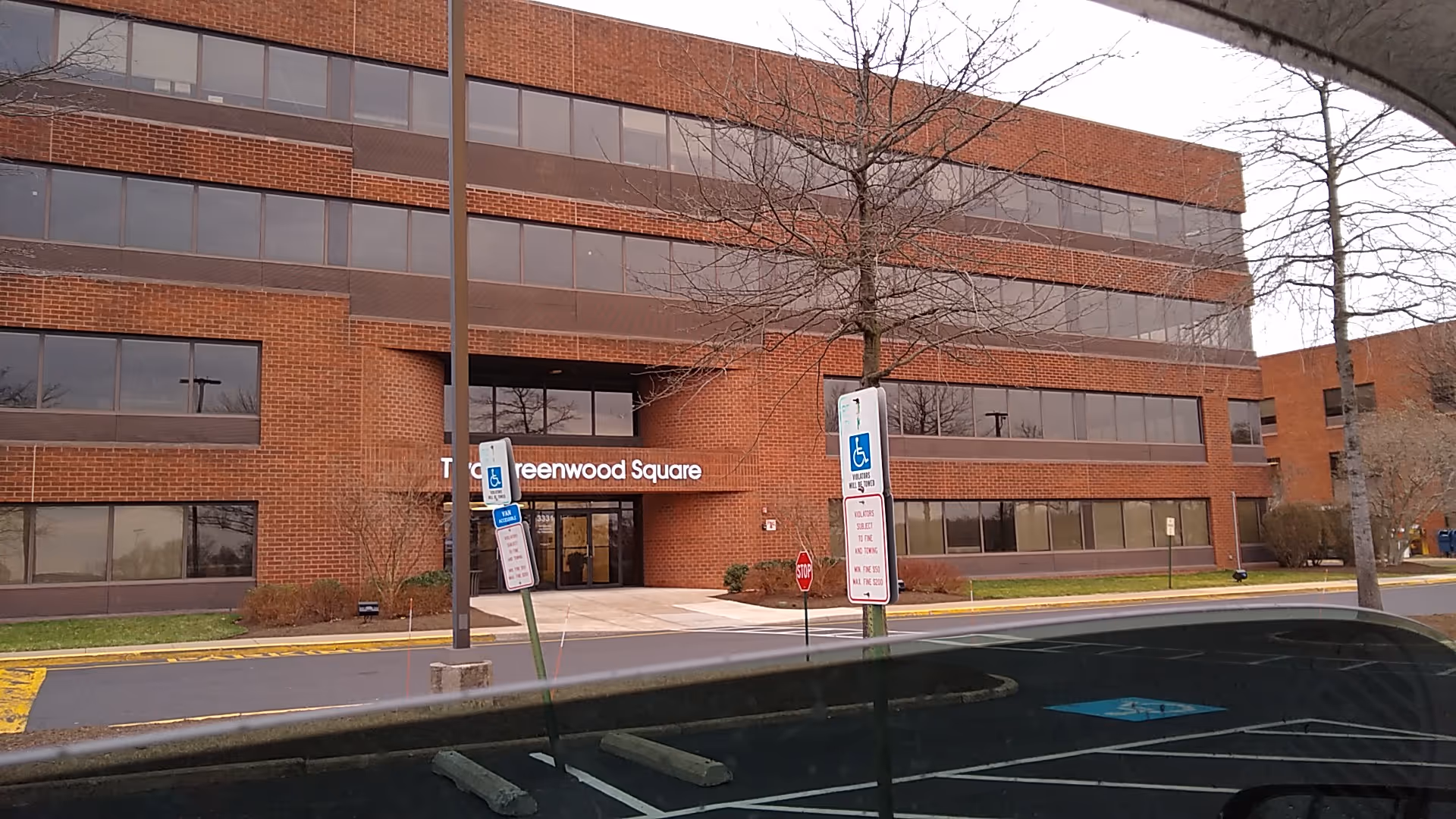 Brick multi-story building exterior with entrance, wheelchair signage, and parking spaces in view.