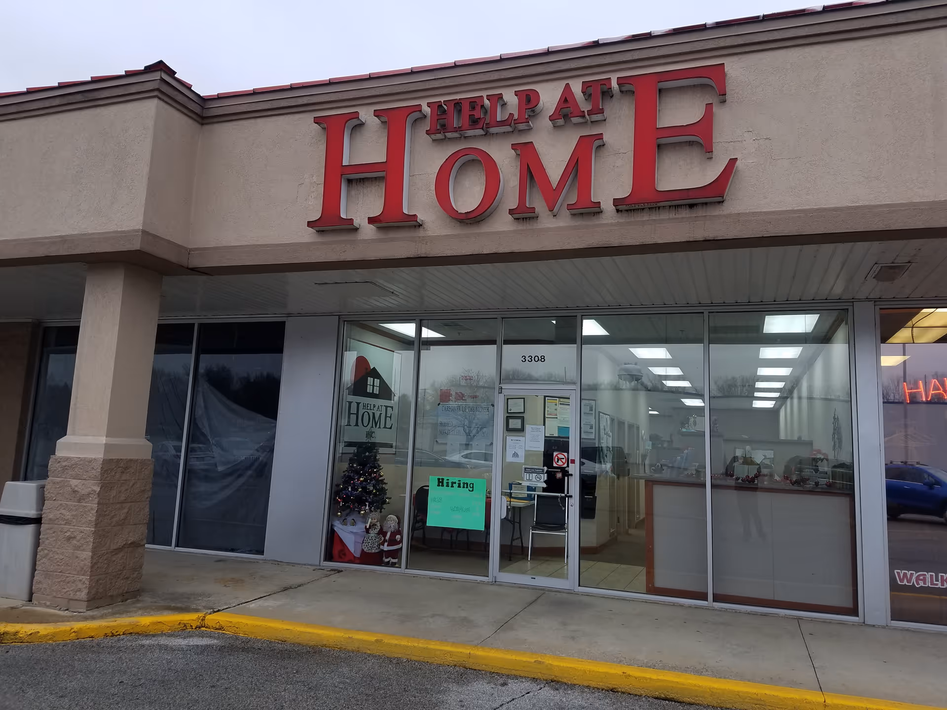 Exterior view of a Help at Home storefront with glass doors and a hiring sign.