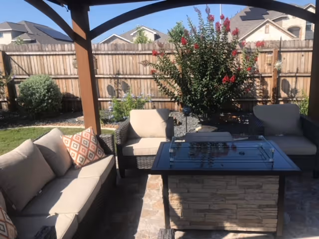 Outdoor covered patio with beige cushioned seating surrounding a stone-fire pit table.