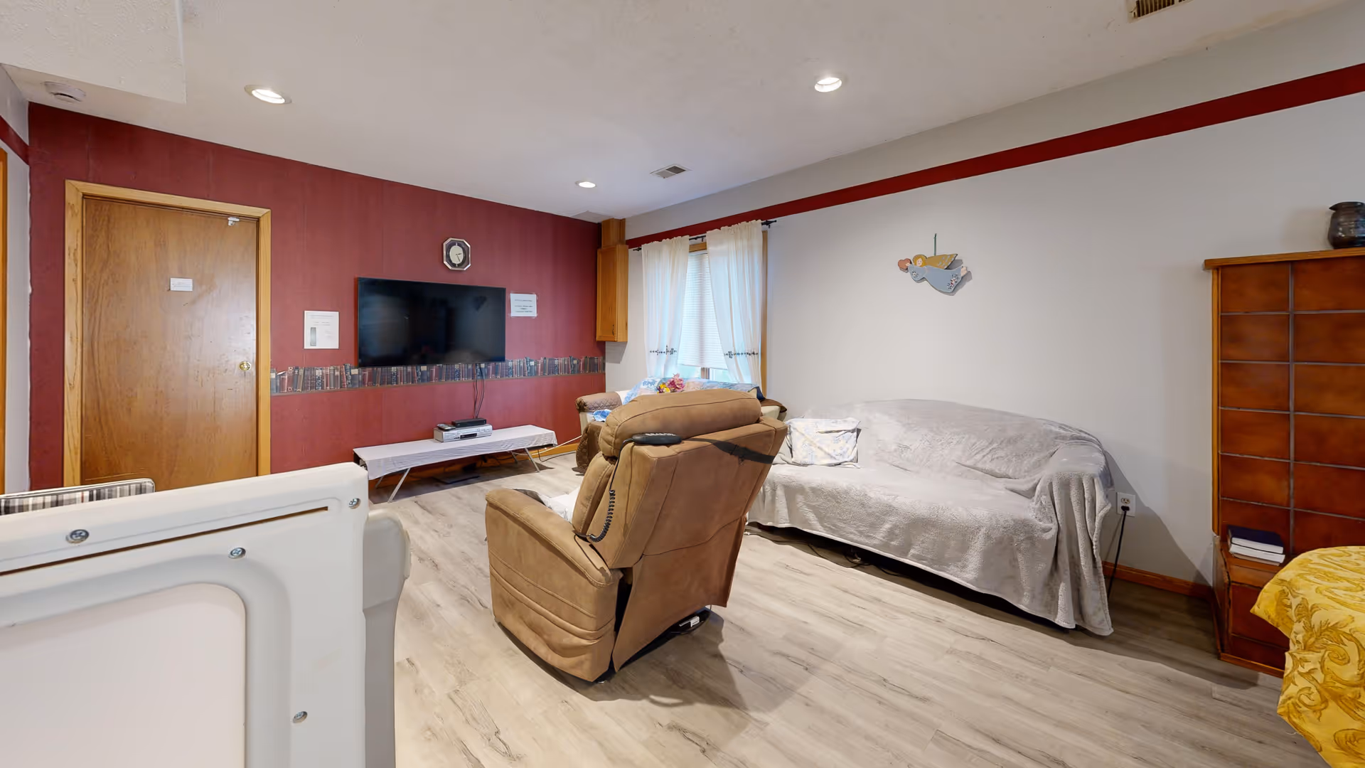 Cozy senior living lounge featuring a TV, two recliners, and a covered sofa.