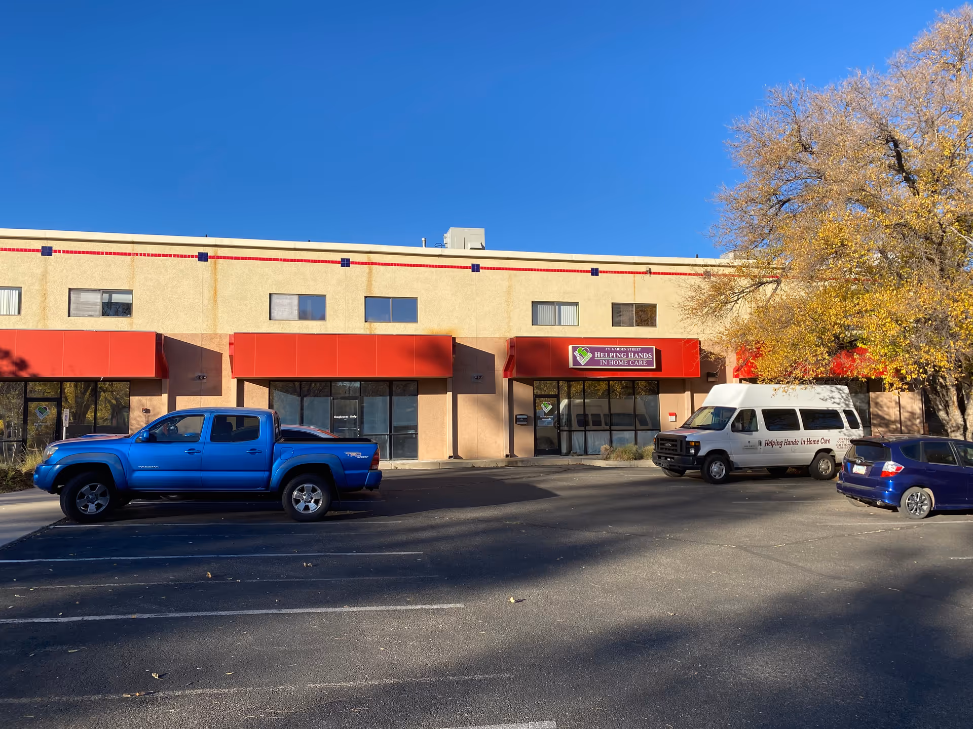 Exterior of a care facility with red awnings and a sign, plus parked vehicles.
