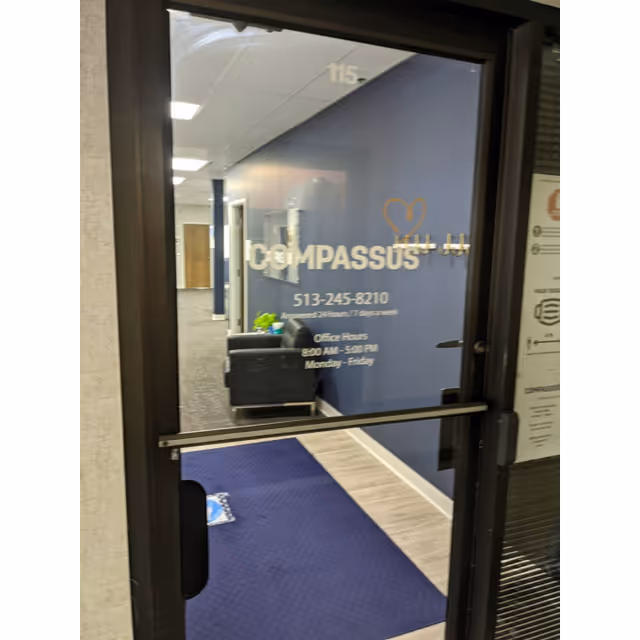 Glass entrance door displays Compassus sign; blue lobby and hallway visible inside beyond.