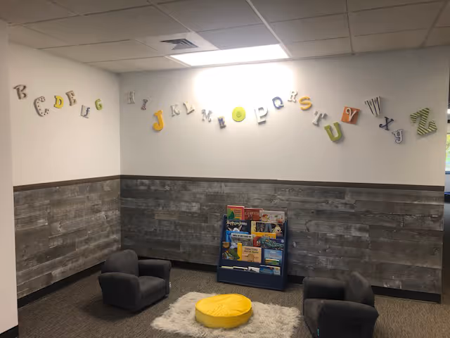 A small lounge area with alphabet wall decor, two chairs, and a yellow cushion on rug.