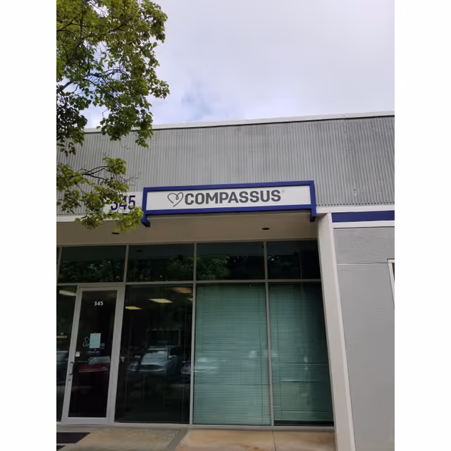 Front entrance of Compassus building with glass doors and a blue and white sign.