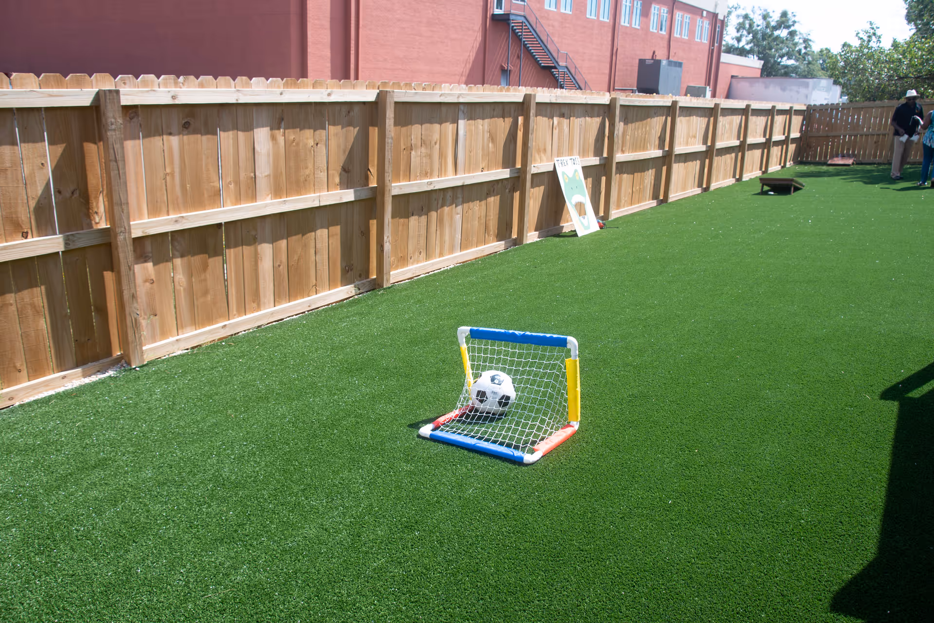 Outdoor artificial turf yard with a small colorful soccer goal and ball near a wooden fence.