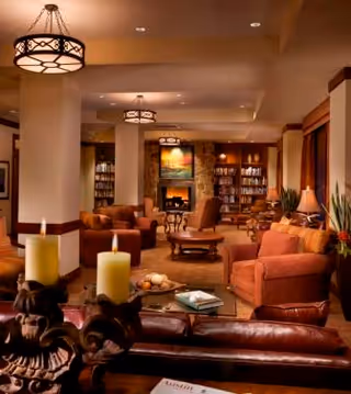 Cozy lounge in a senior living facility featuring sofas, a fireplace, lamps, and bookshelves.