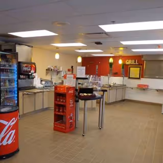 Cafeteria-style dining area with beverage machines and service counter in a senior facility.