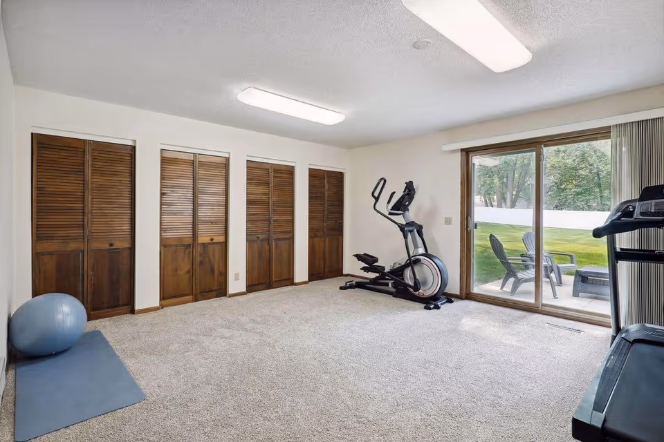 Indoor exercise room with elliptical, treadmill, closets, mat, and sliding glass door to the patio.