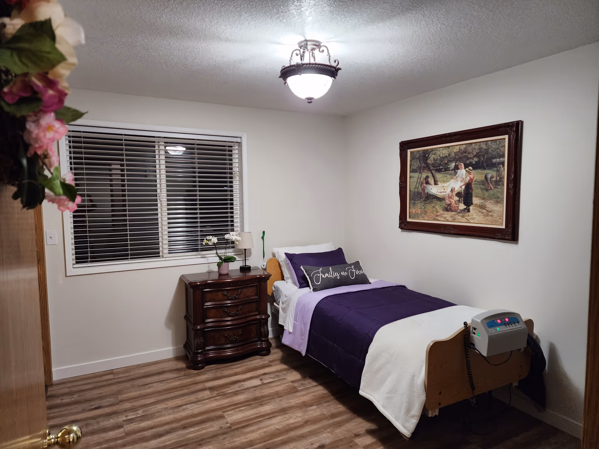A bedroom in a senior care facility featuring a purple bed, dresser, and wall art.