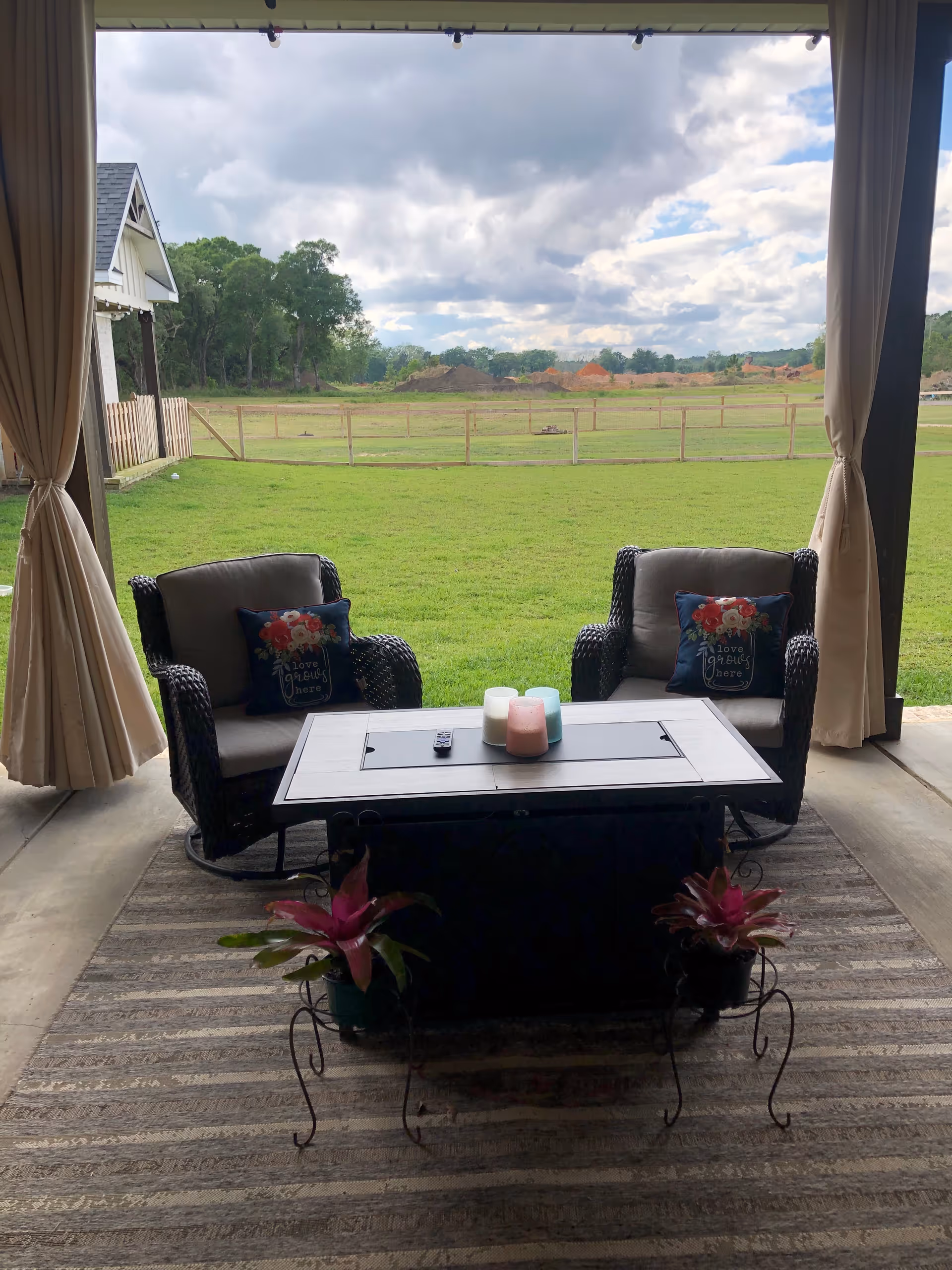Covered outdoor patio with two cushioned chairs, a central coffee table, and green field view.