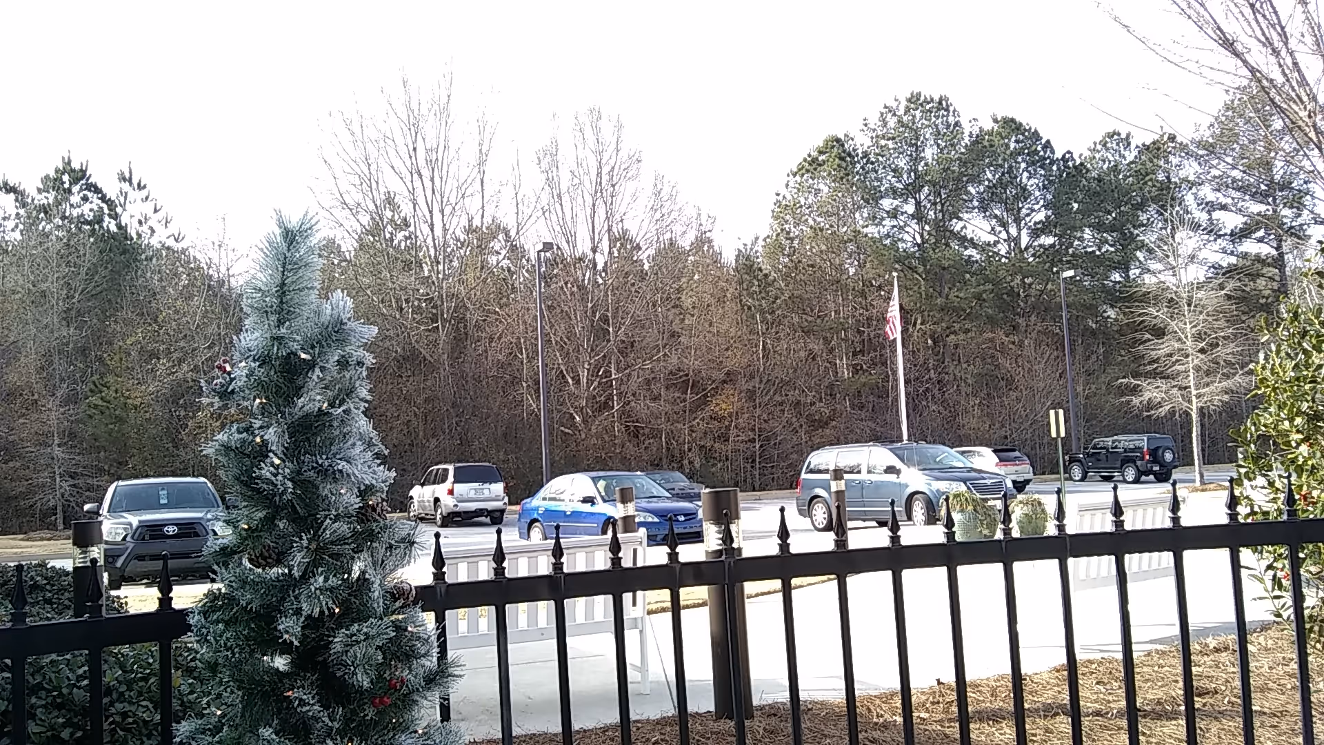 Exterior view of a gated parking lot with several cars and leafless trees in the background.