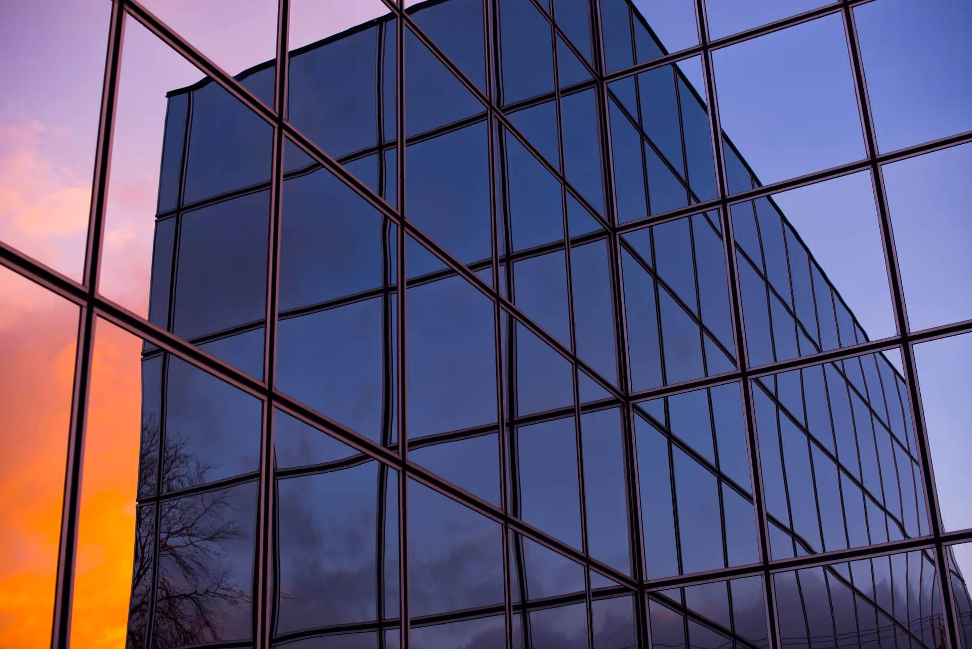 Glass-paneled building facade reflects a colorful sunset across its windows.