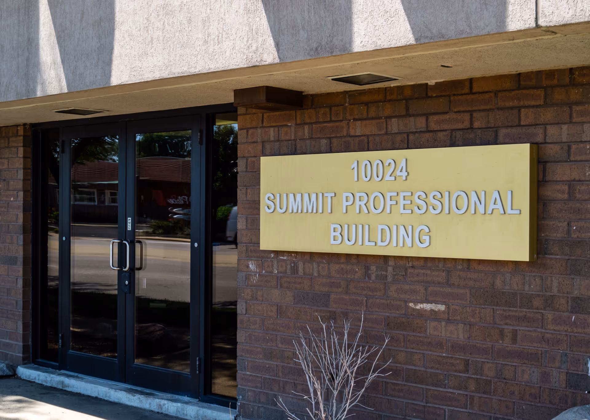 Brick building entrance with glass doors and a yellow sign reading Summit Professional Building.