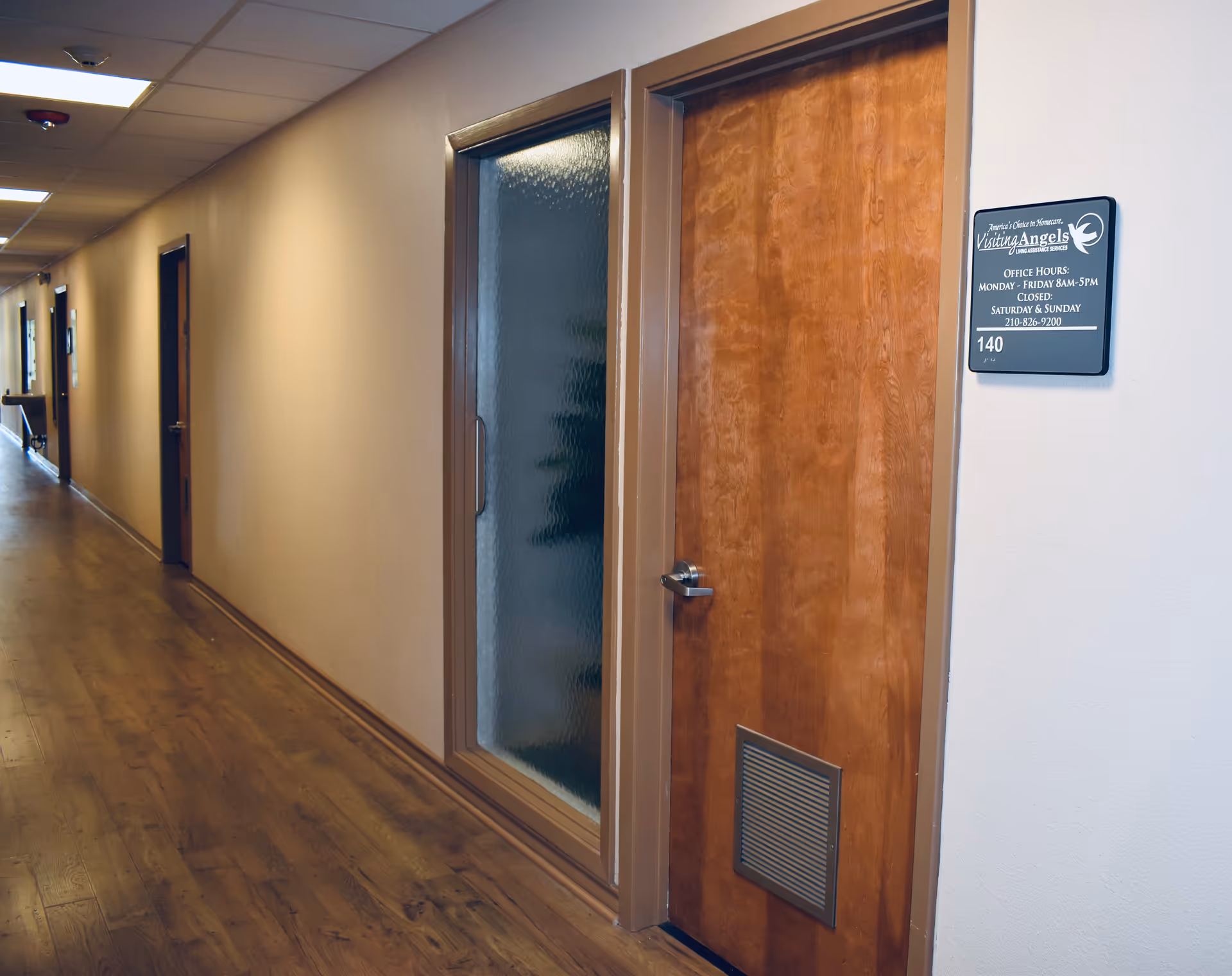 Long, well-lit hallway inside a senior living facility with wooden floors and doors.