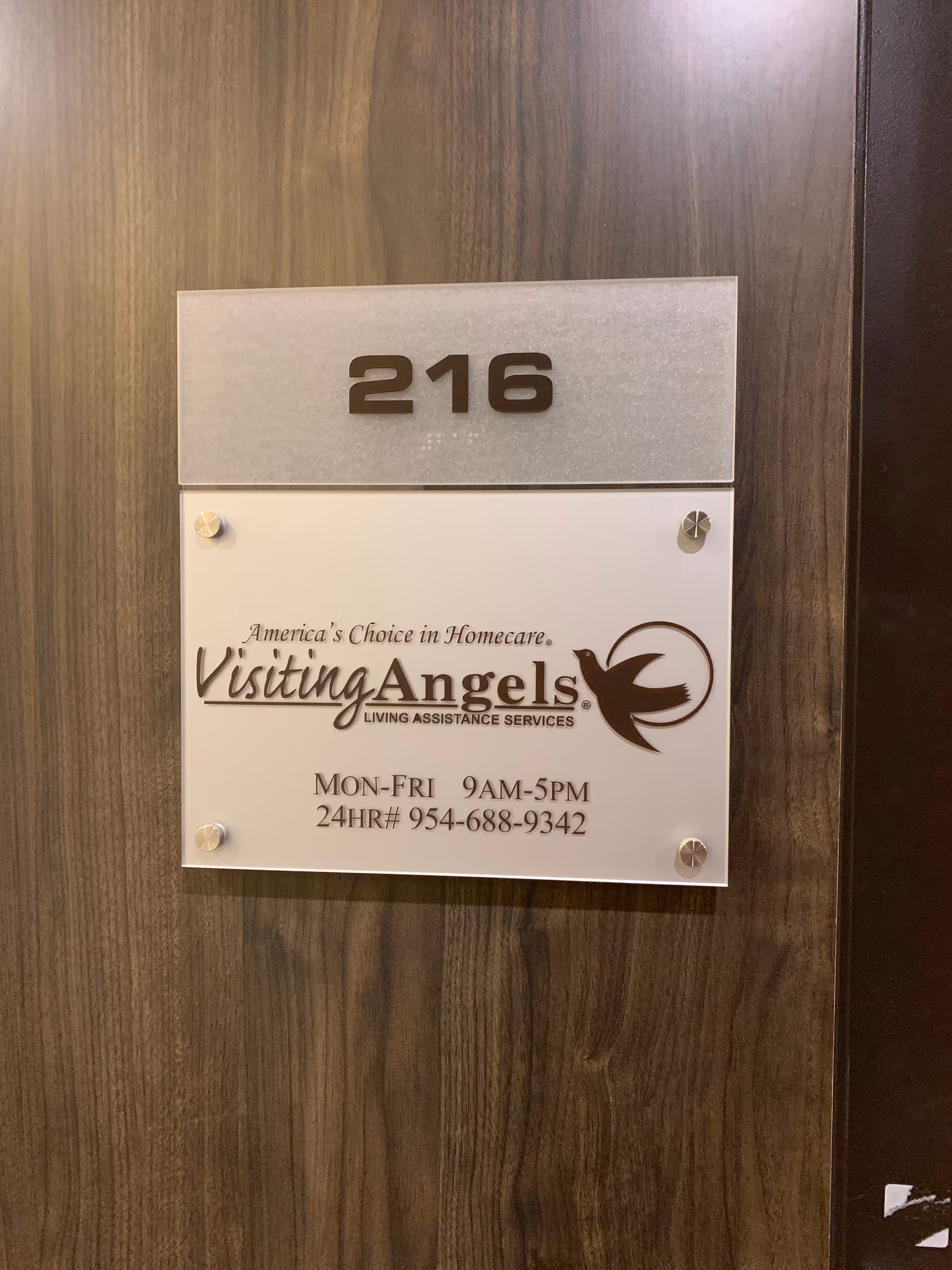 Door plaque shows room 216 and Visiting Angels sign on wood-paneled wall.