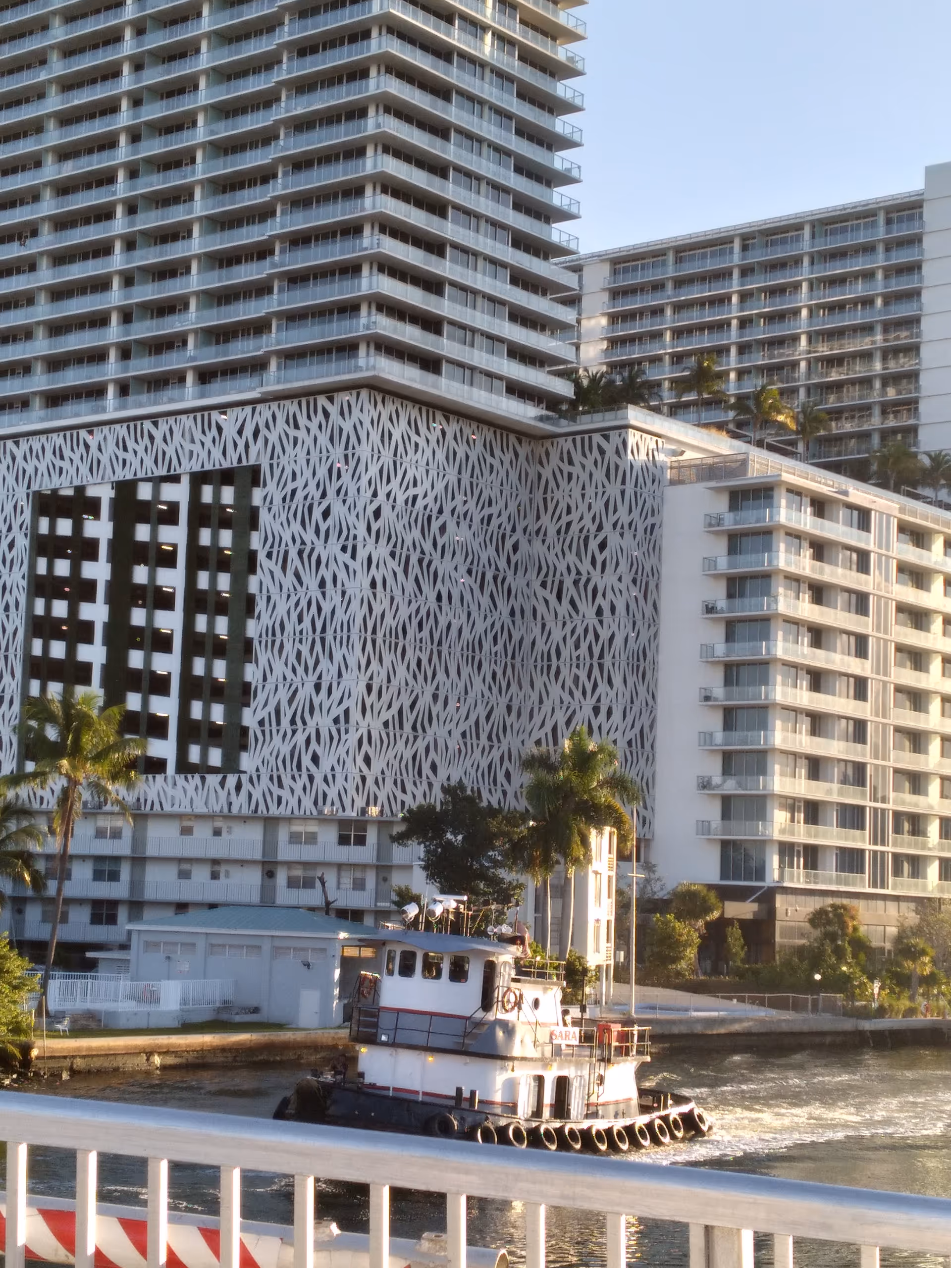 Modern waterfront buildings with palm trees and a small boat near the riverfront.