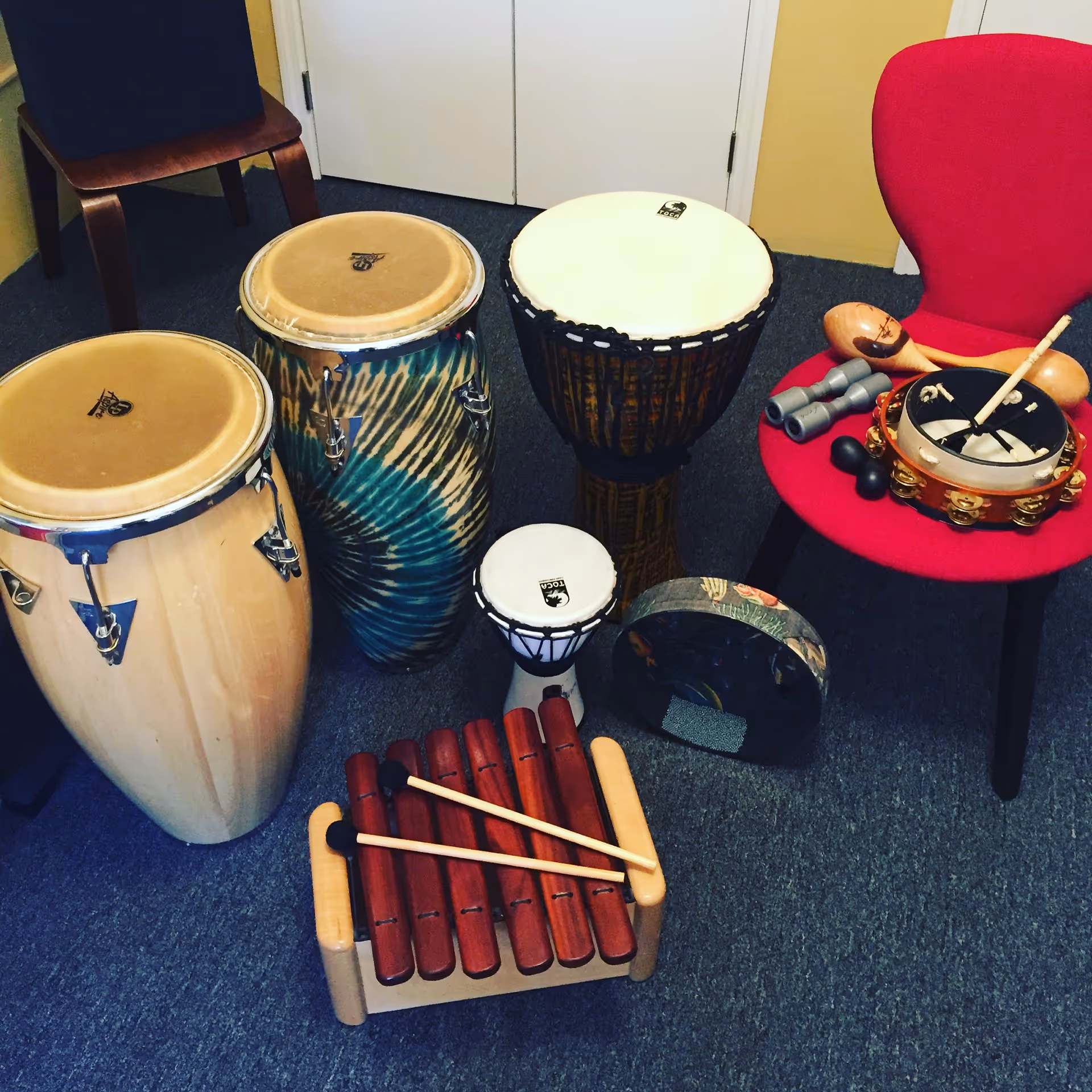 A music therapy room with congas, drums, a xylophone, and a red chair.