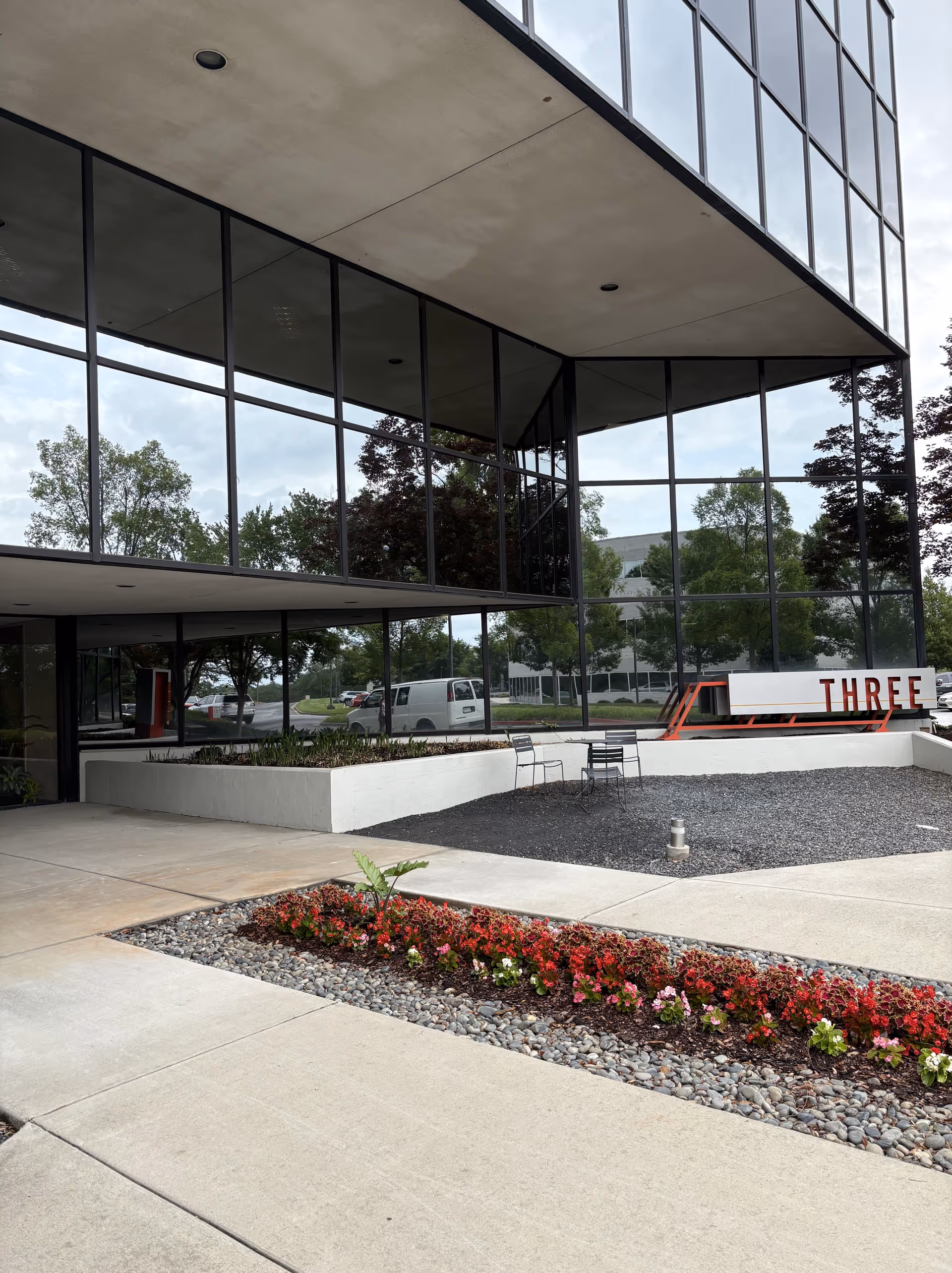 Modern glass-front building exterior with landscaped entry and outdoor seating.