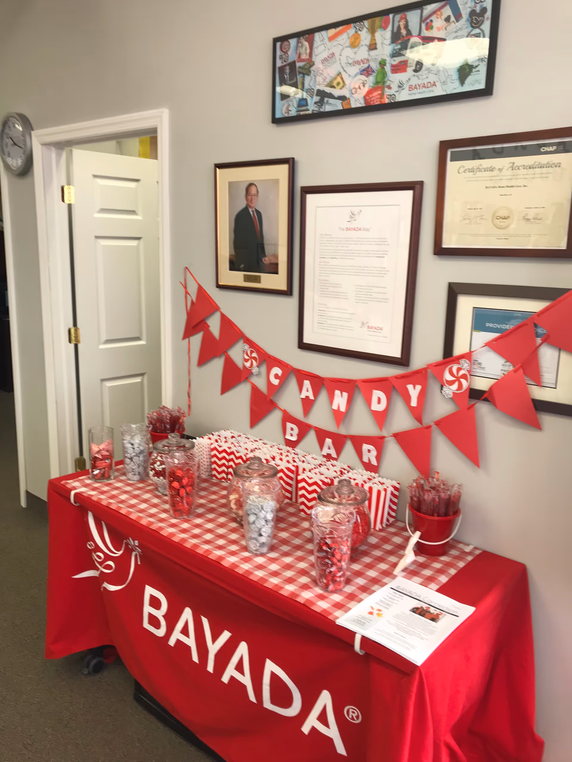Red BAYADA candy bar setup on a decorated table with framed certificates on the wall.