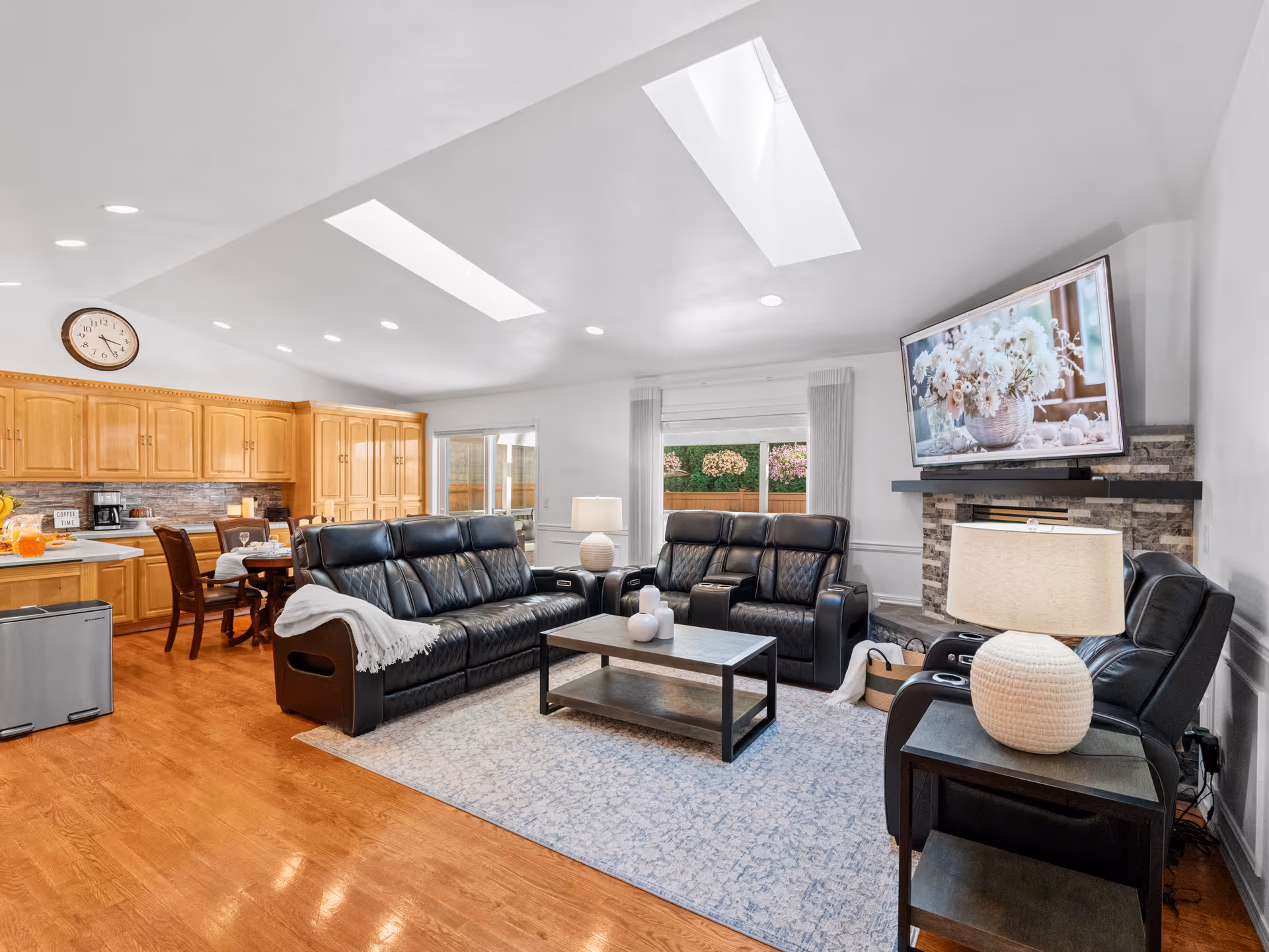 Open plan living room with leather sofas, coffee table, fireplace, and kitchen at back.