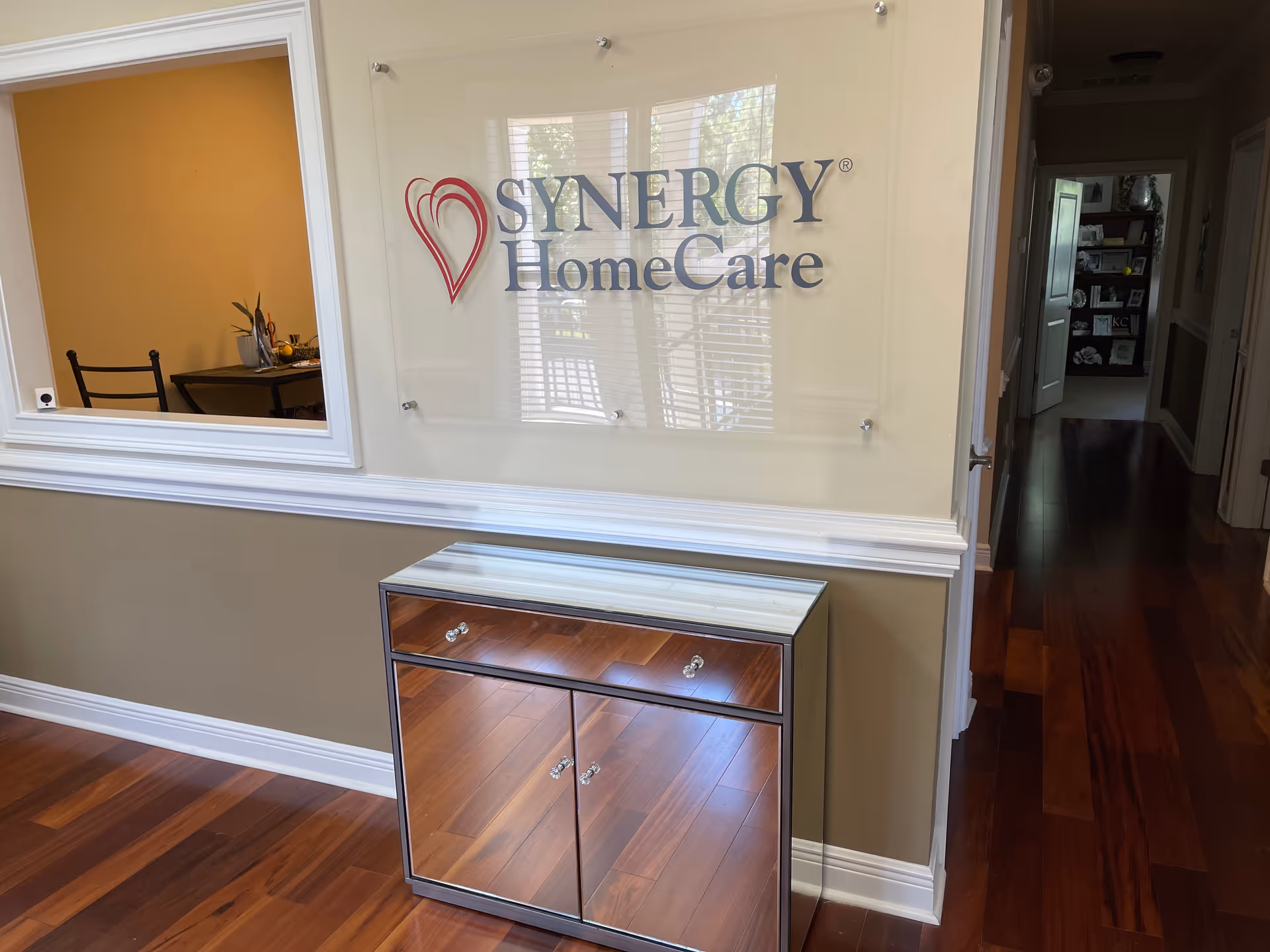 Interior hallway with Synergy HomeCare sign on glass panel, wood floor, and cabinet.