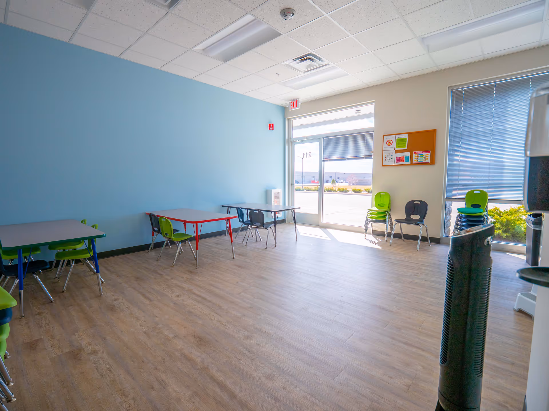Bright, empty indoor activity room with tables and colorful chairs by the windows.