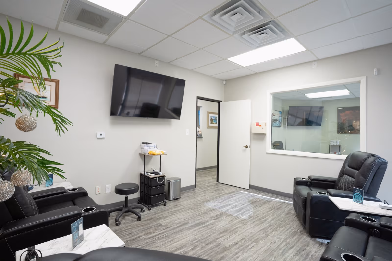 Modern lounge in a senior living facility with reclining chairs, TV, and plants.