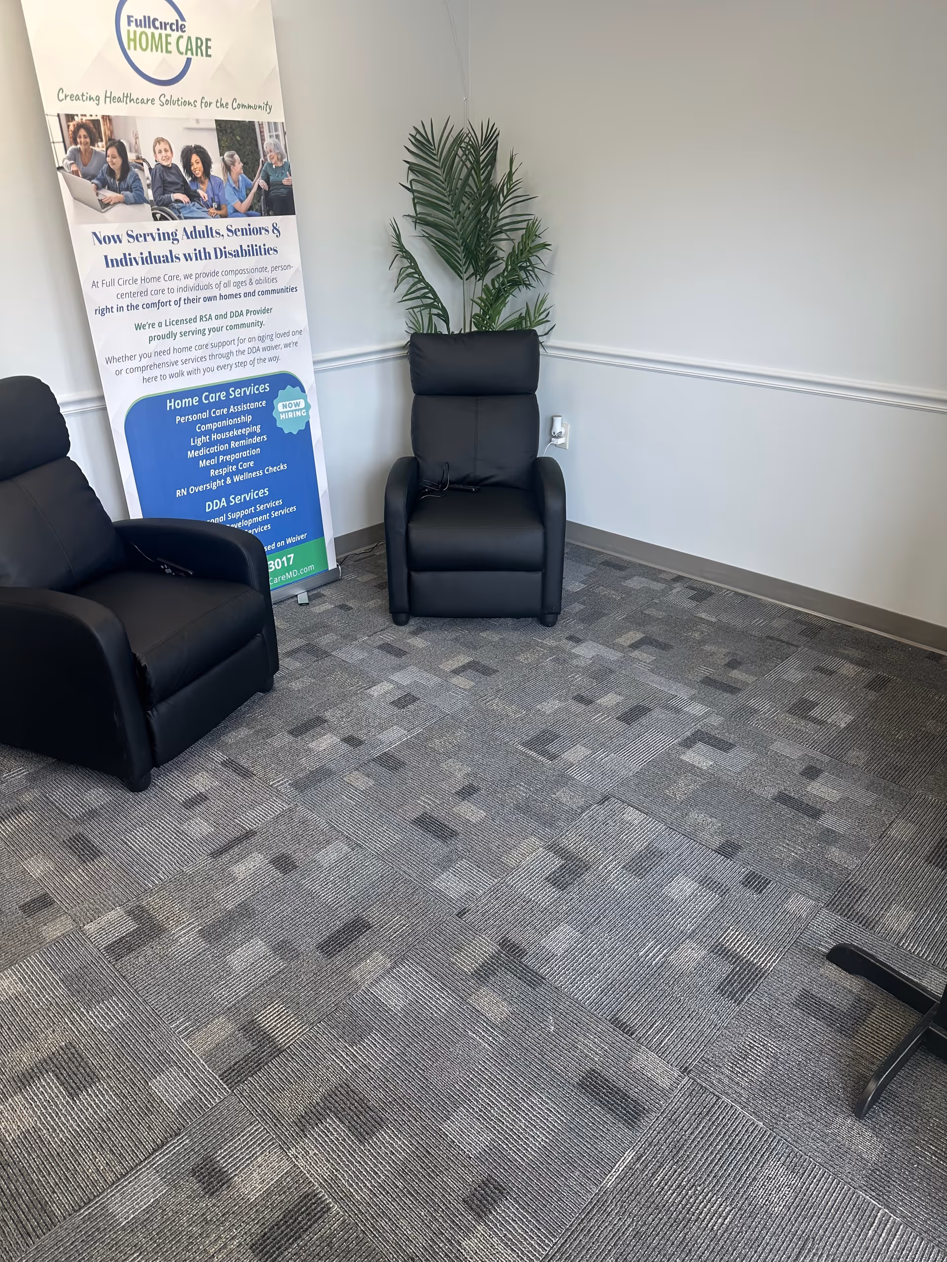 A small interior waiting area with black chairs, a banner, and a tall plant.