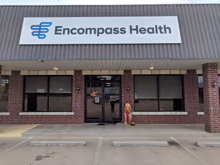 Brick storefront with Encompass Health sign and glass entrance doors under a storefront awning.