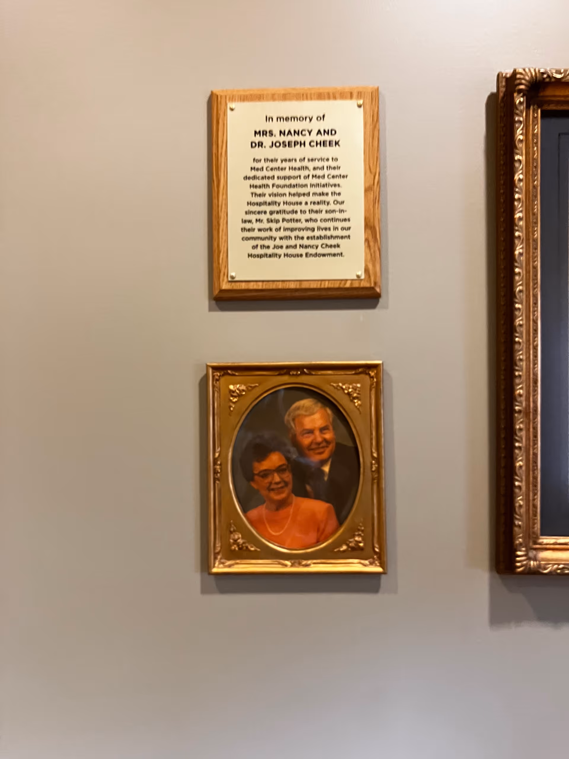 Wall display with a memorial plaque and framed portrait of a couple.