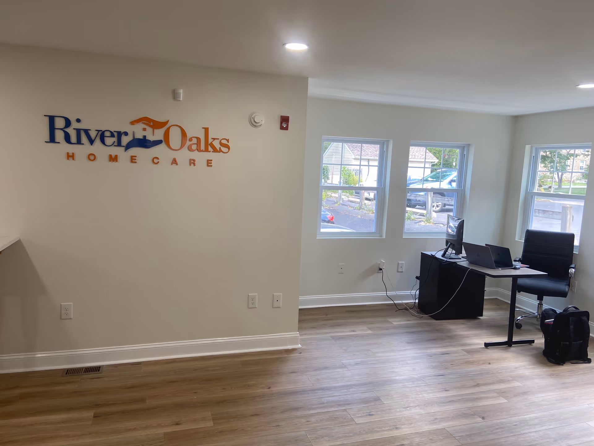 Office reception area inside River Oaks Home Care with desk, computer, and logo wall.