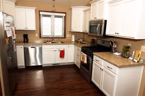 Bright white kitchen with stainless steel appliances, granite countertops, and dark wood flooring.