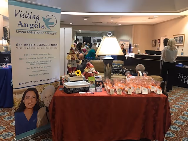 Indoor lobby with a Visiting Angels banner and a red-draped display table.