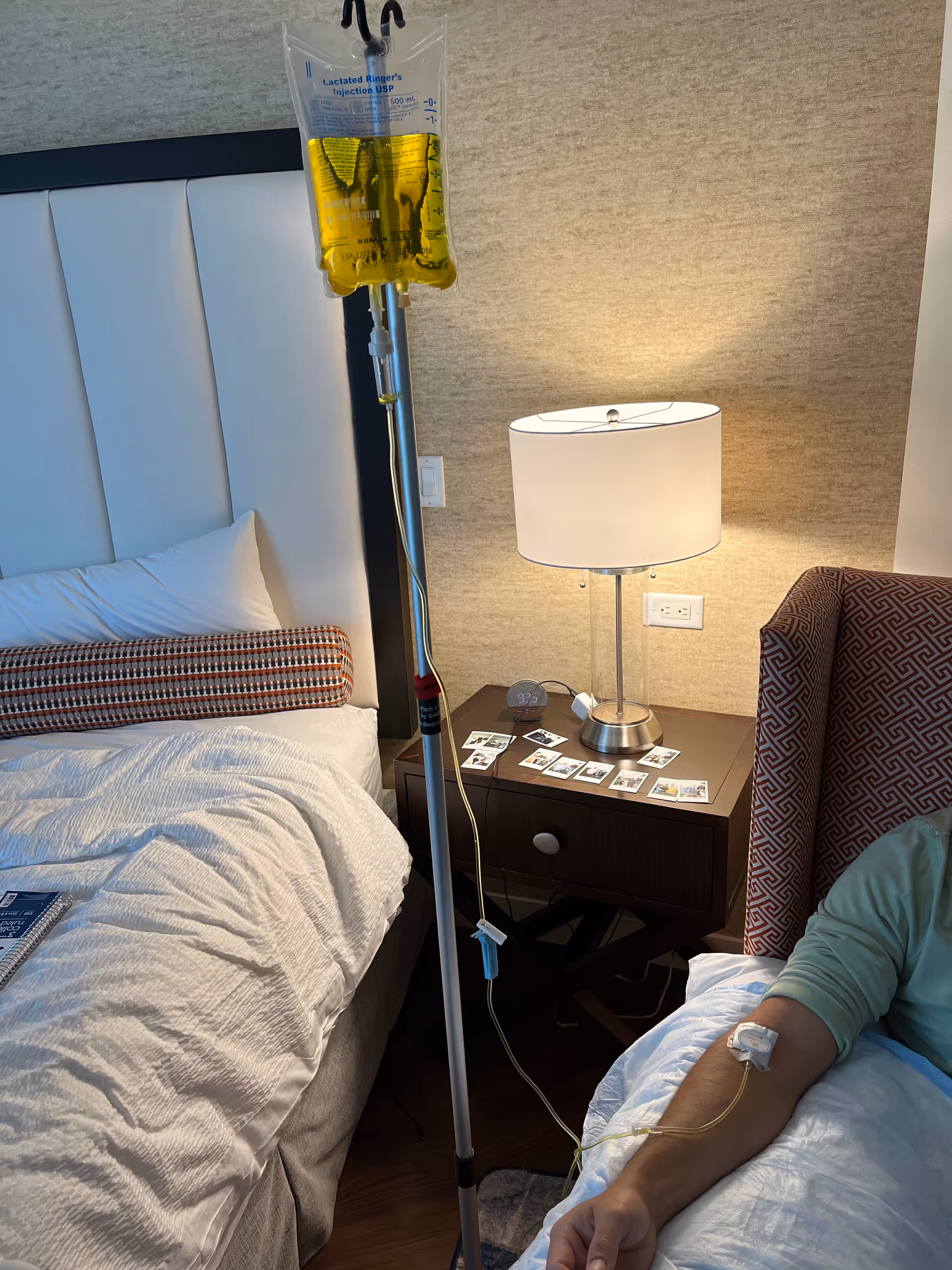 IV drip bag and stand beside a bed in a modern hotel-style patient bedroom.