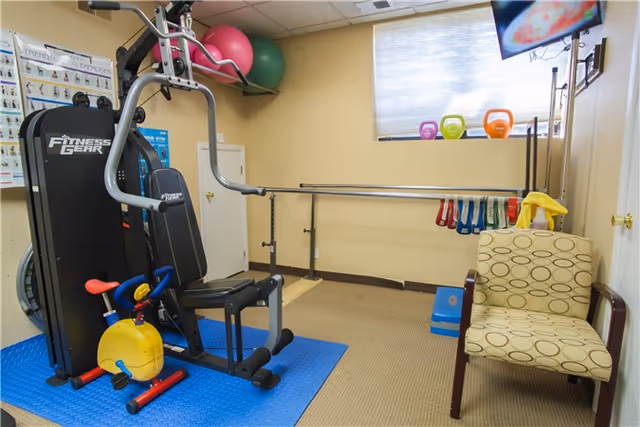 Small physical therapy gym with exercise equipment, a chair, and therapy accessories.