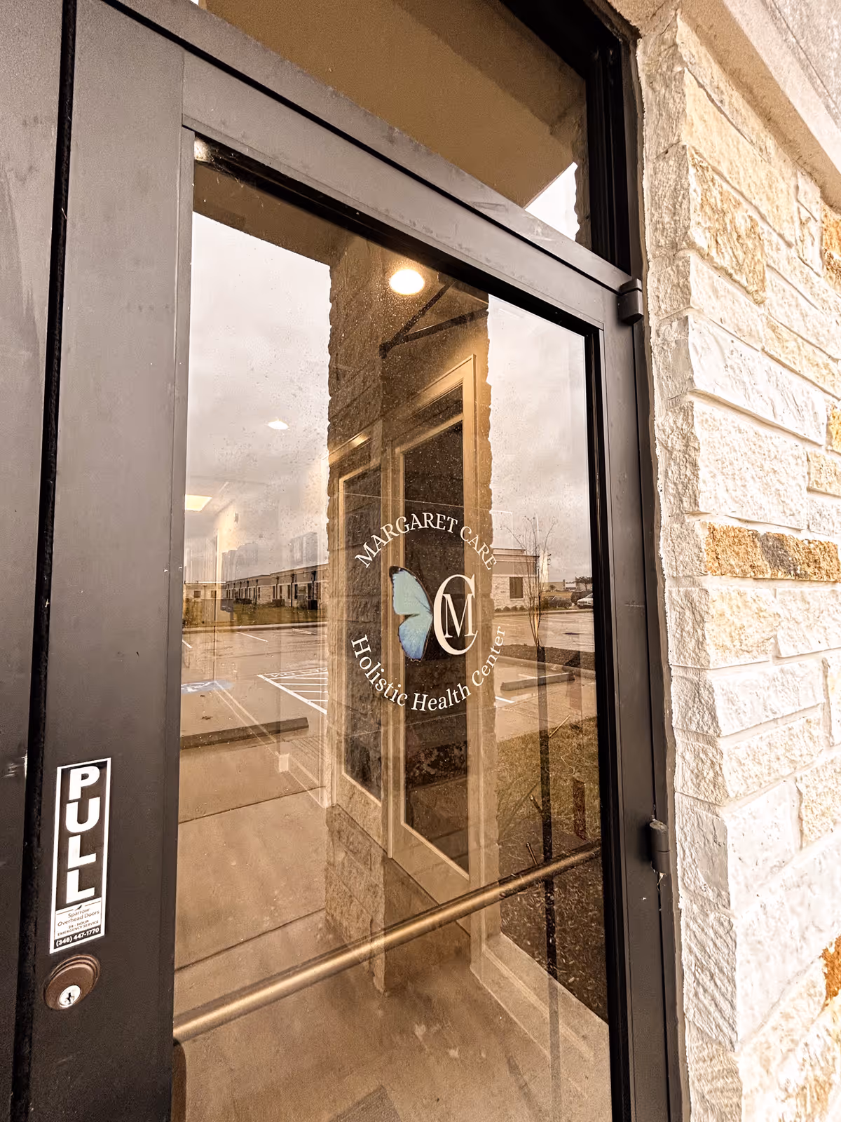 Glass entrance door with MargaretCare logo against a stone exterior wall