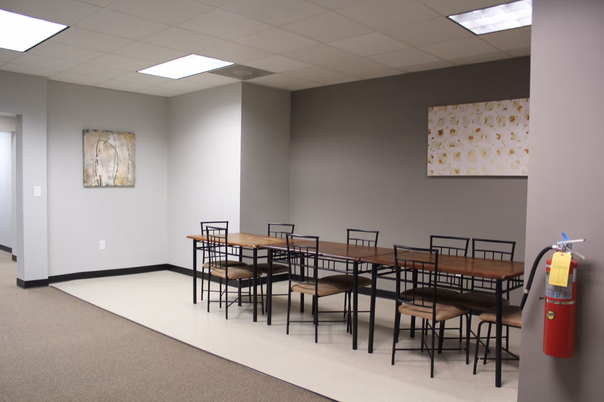 A long wooden dining table with metal chairs in a neutral senior living facility dining area.