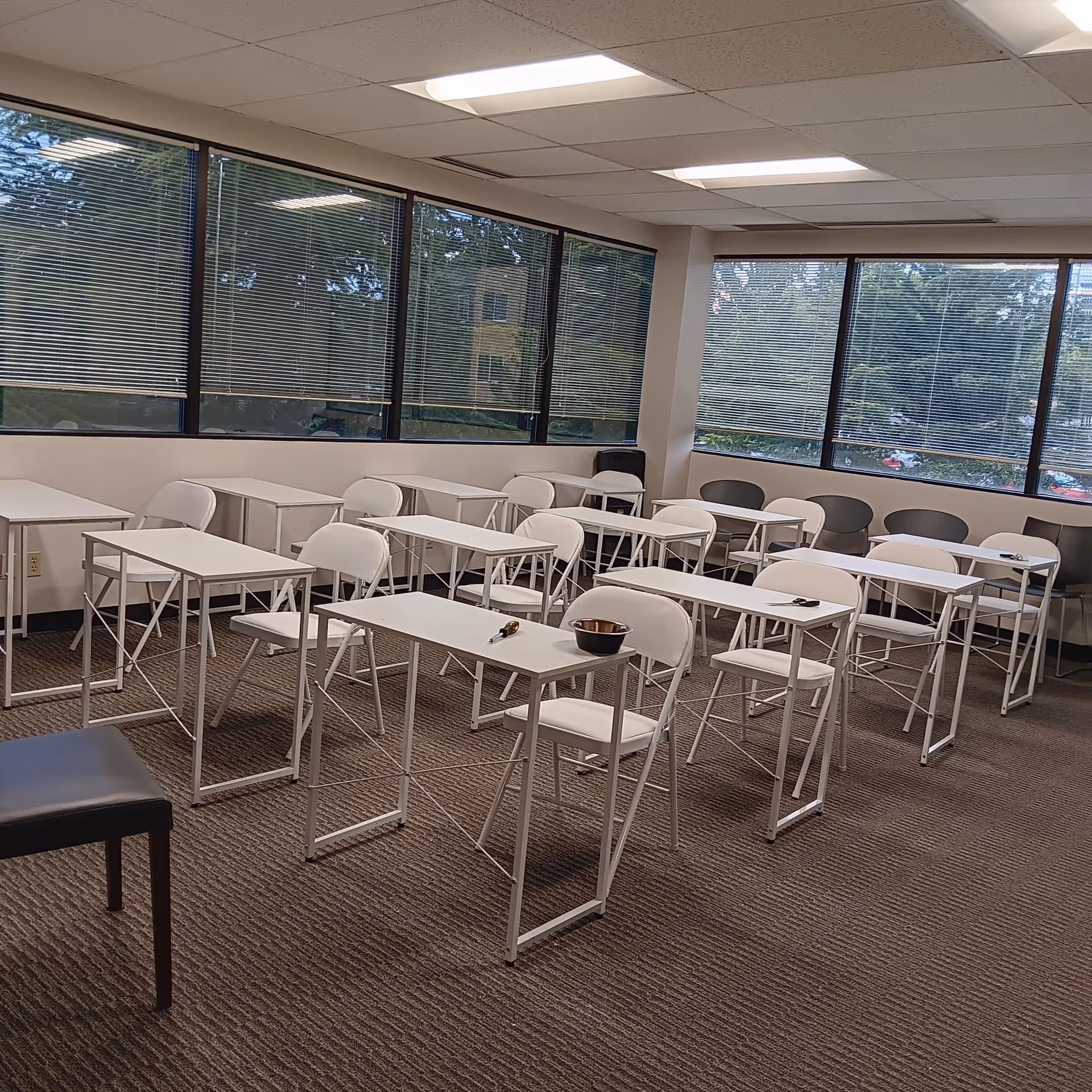 Bright training room with white desks and chairs arranged in rows near large windows.