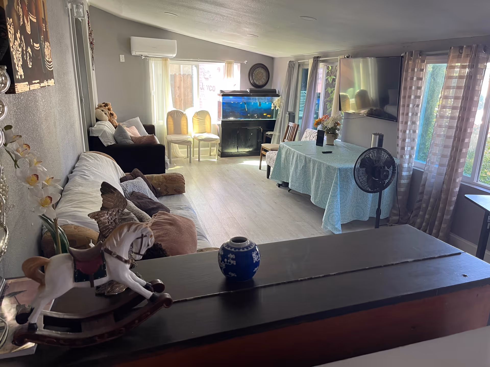 Bright living room with sofa, dining table, aquarium, and large windows in soft decor.