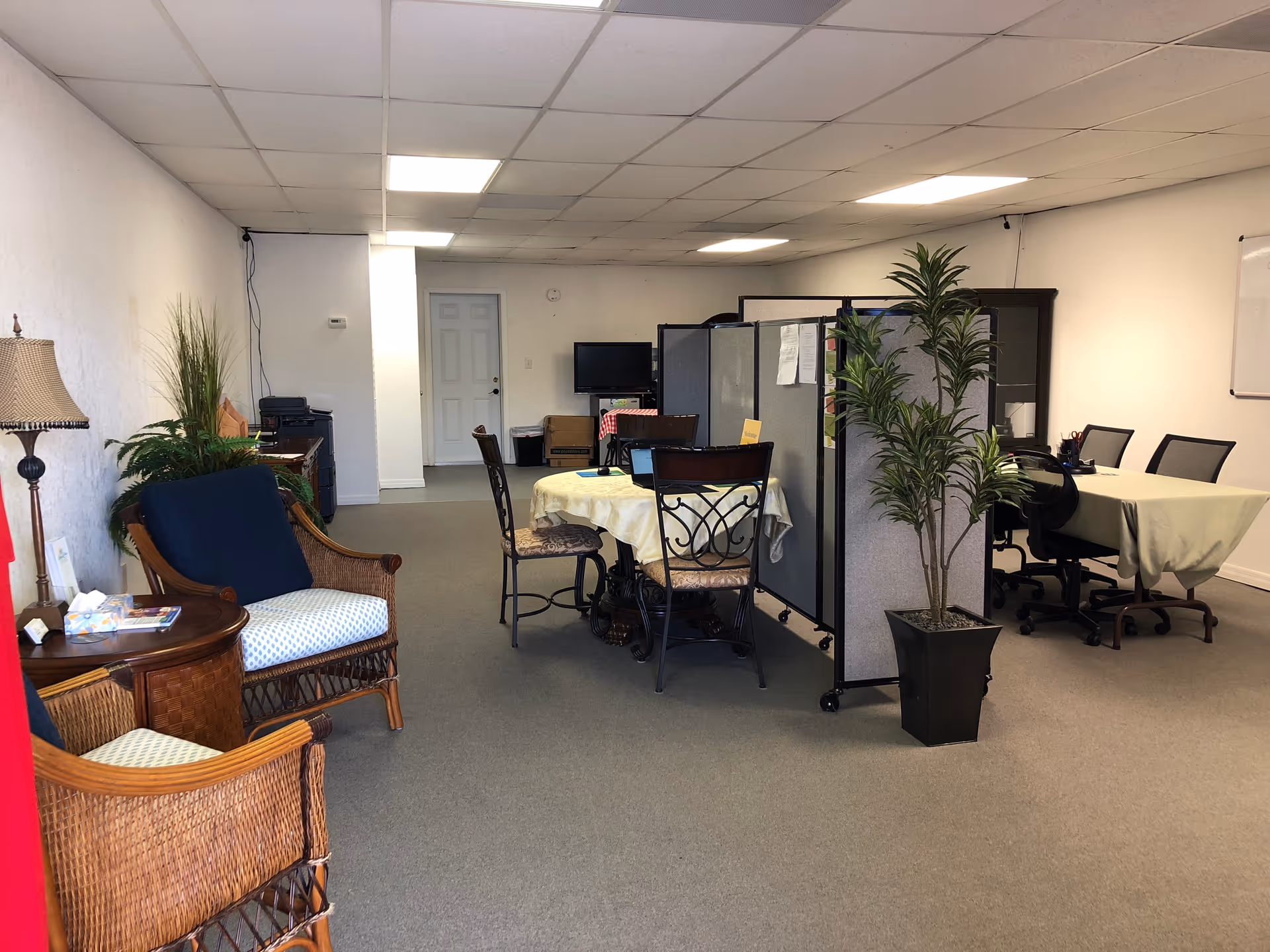 Interior common area with round tables, cubicles, wicker chairs, and potted plants.
