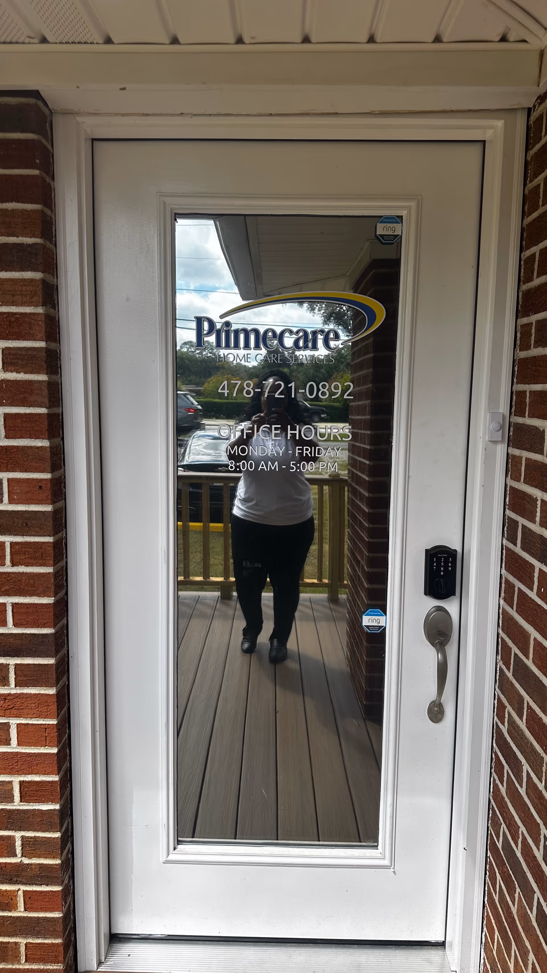 Glass door of Primecare Home Care Services with office hours; brick exterior and reflection.