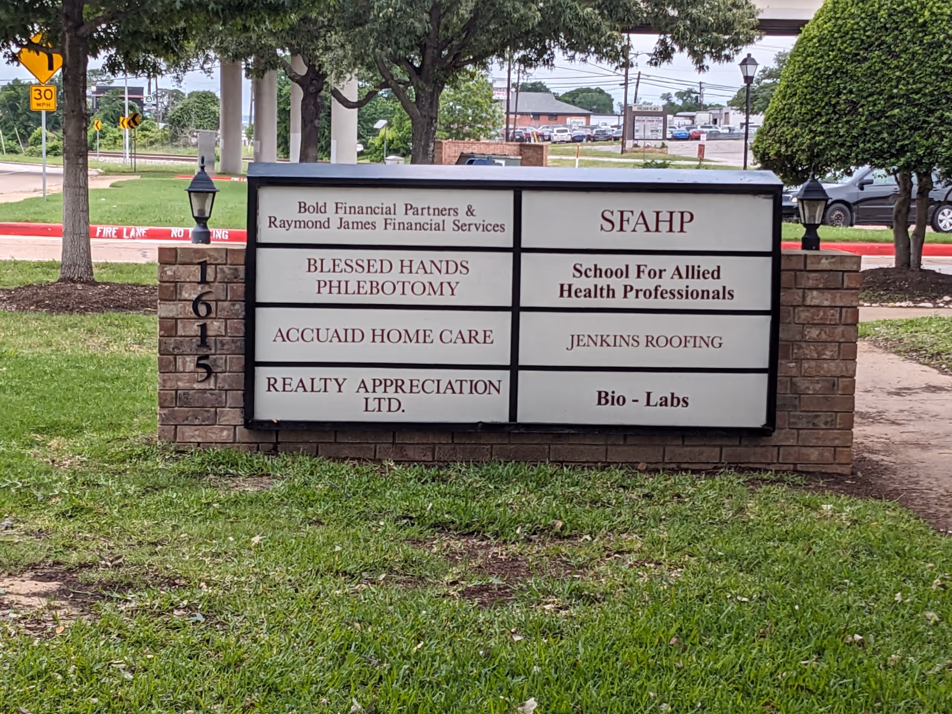 Exterior signboard displaying multiple business names, including AccuAid Home Care, on brick base.