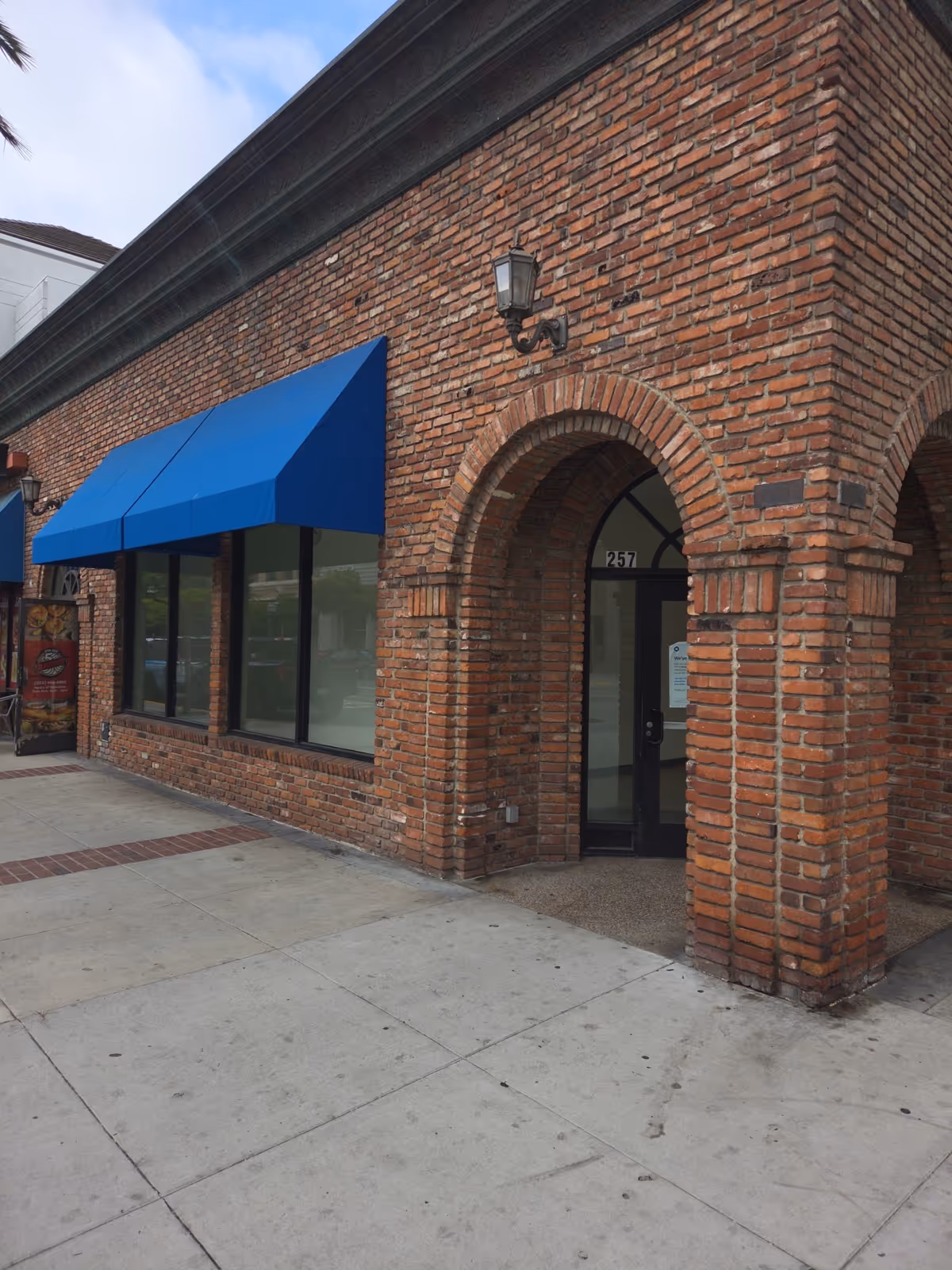 Brick building exterior with arched doorway and blue storefront awning along sidewalk.