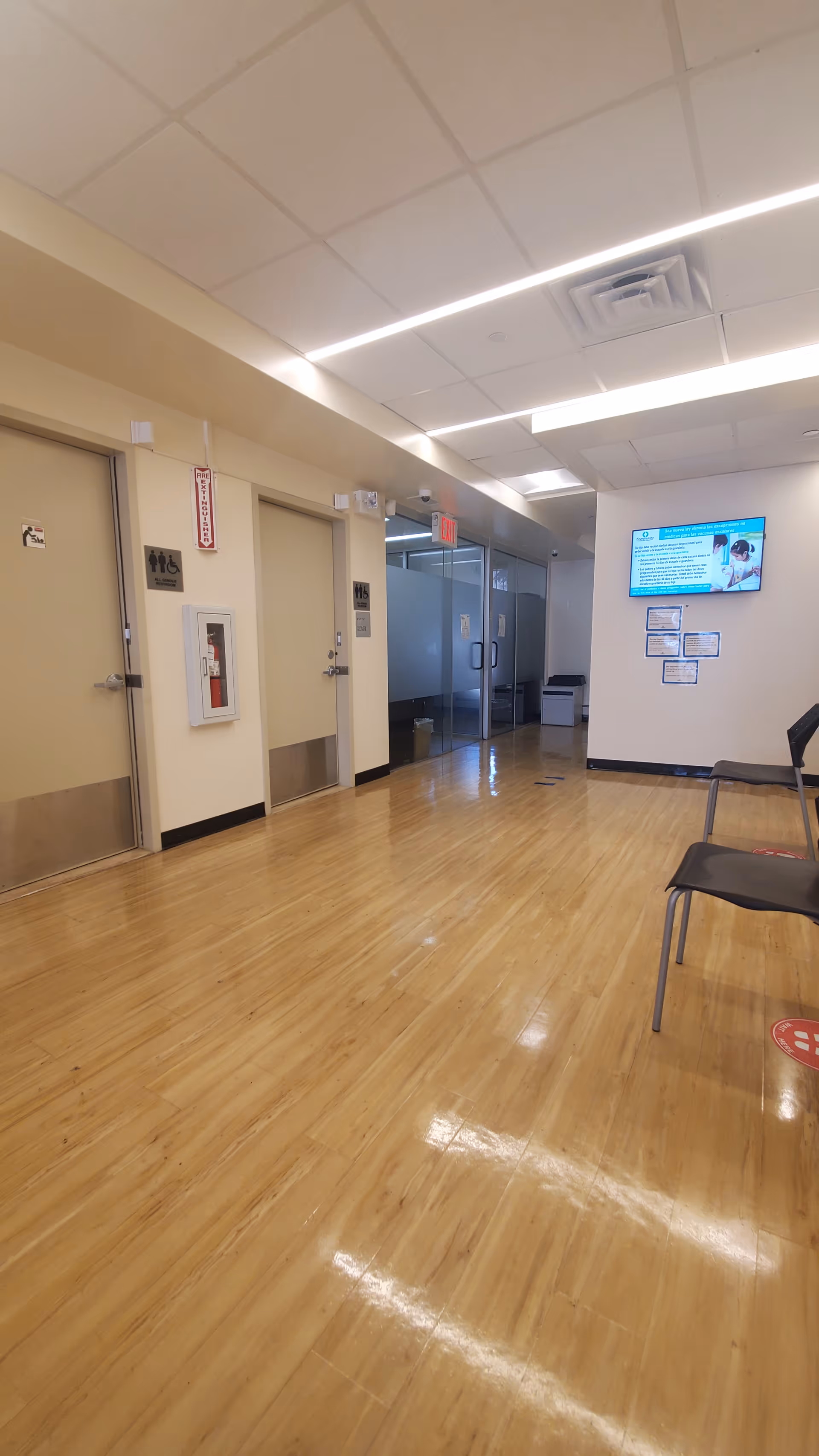 Long polished hallway inside a senior living facility with doors, chairs, and a wall-mounted screen.