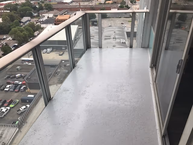 High-rise balcony with glass railing overlooking a parking lot and city streets.