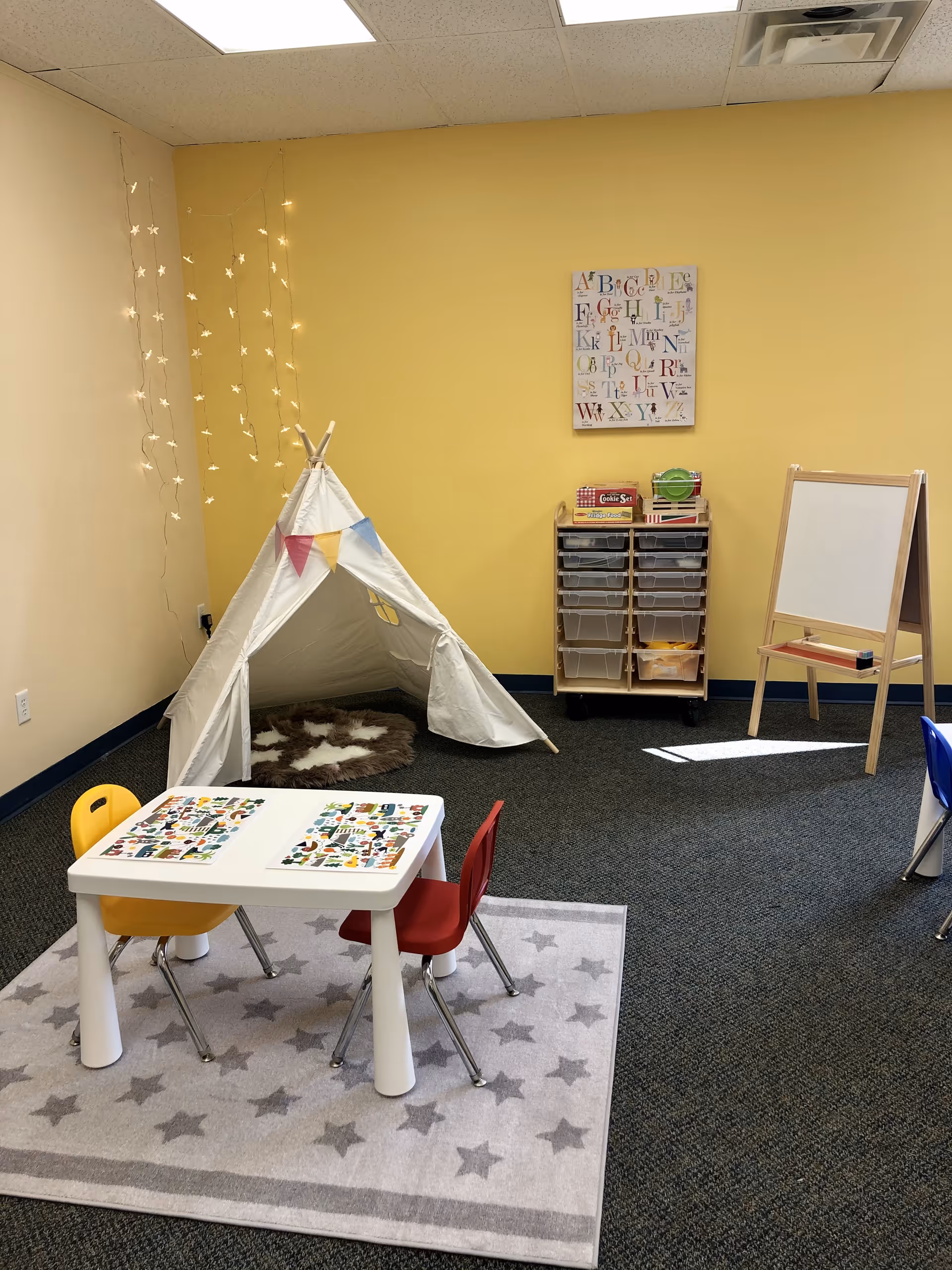 Yellow-walled indoor playroom with a small tent, star rug, and child-sized furniture.