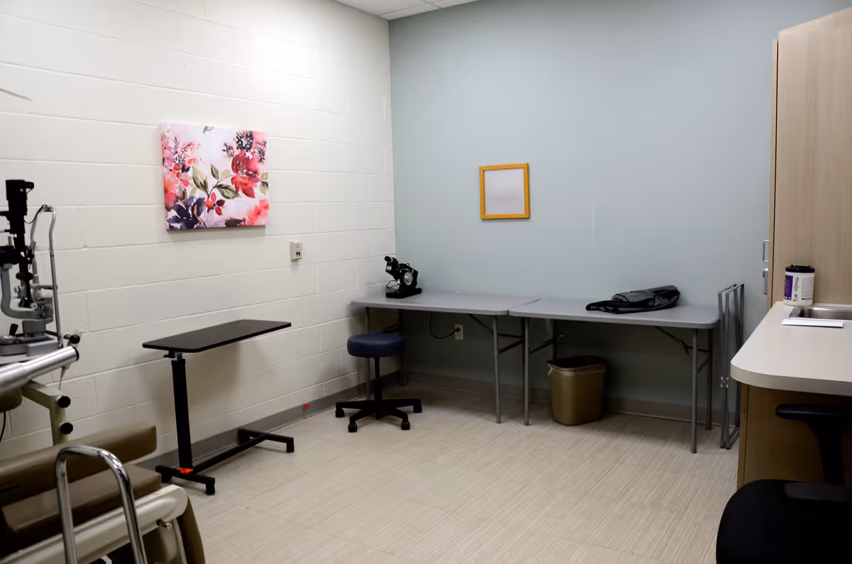 Clinical examination room in a care facility with medical equipment and seating.