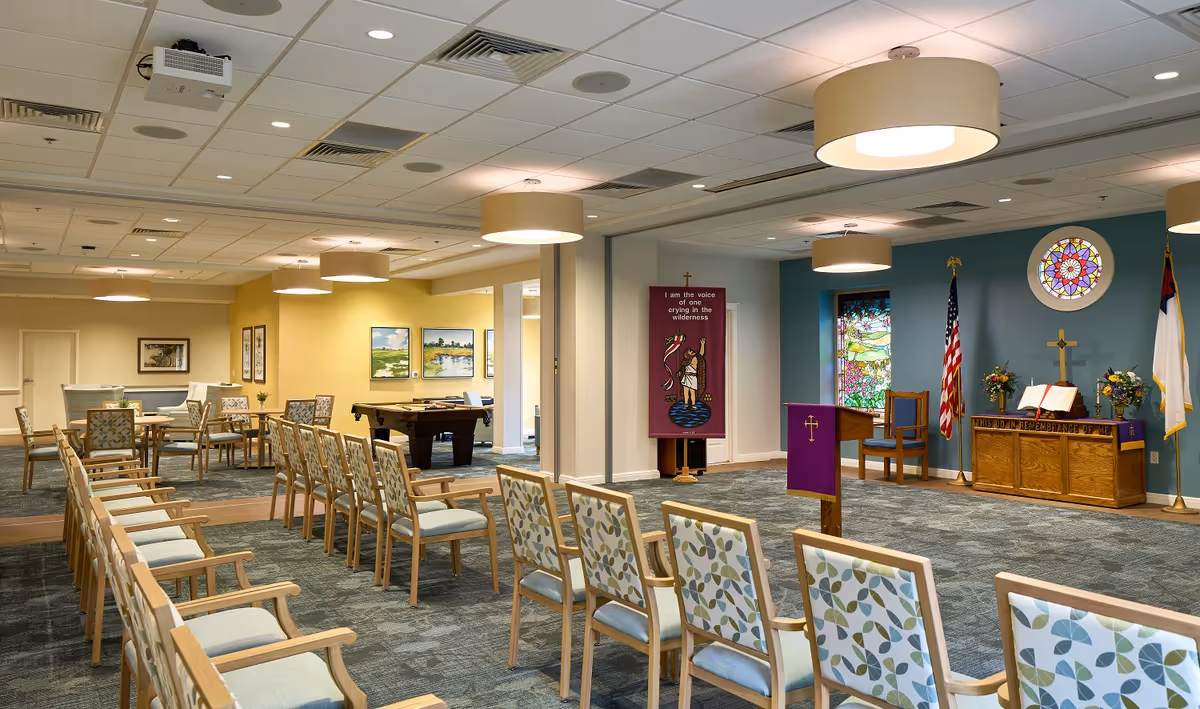 Chapel area of a senior living facility with arranged chairs, pulpit, flags, and stained glass